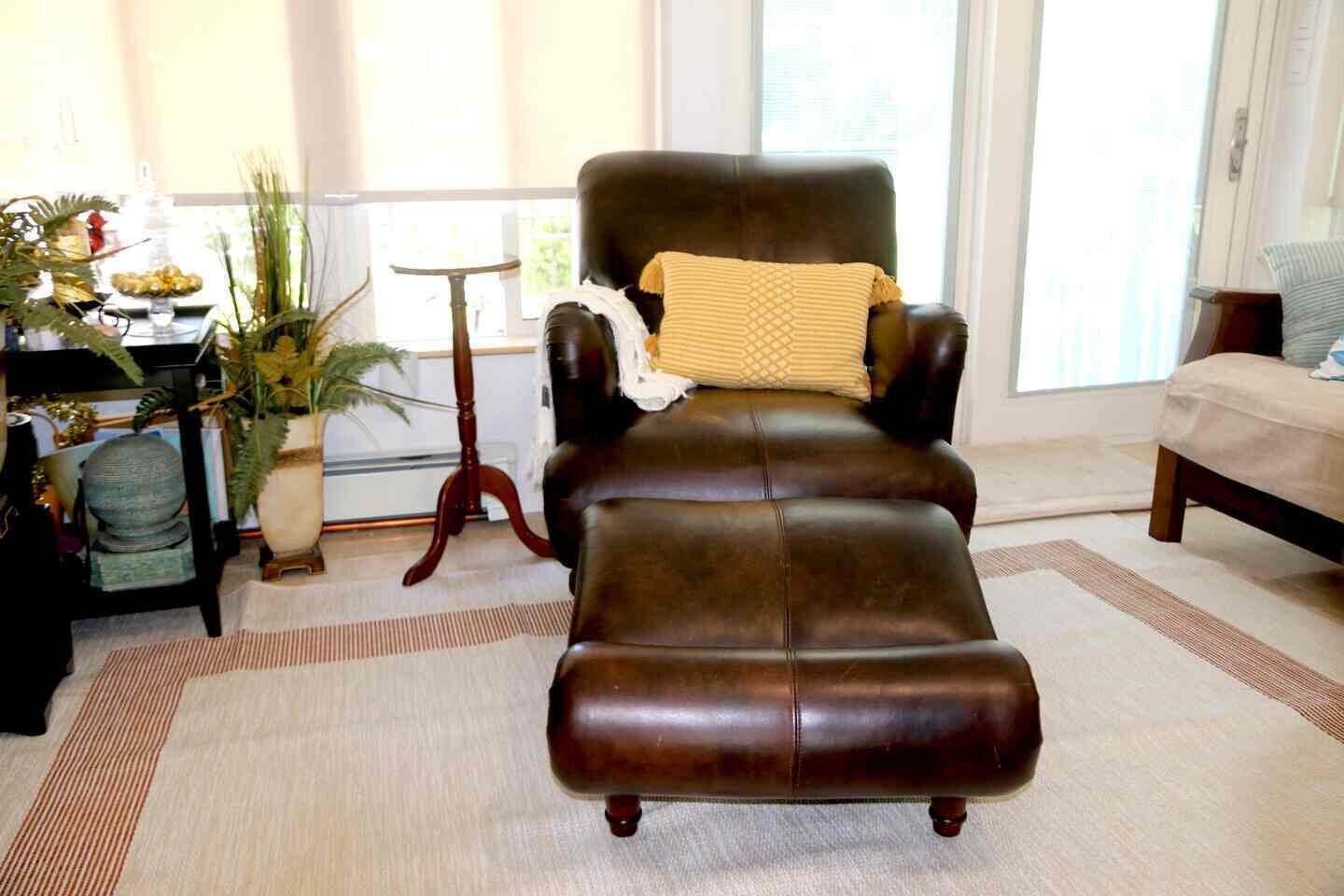A leather armchair with a cushion, a small table, and a potted plant in a room with a large window.