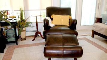 A leather armchair with a cushion, a small table, and a potted plant in a room with a large window.