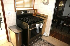 A kitchen with a stove, oven, and a trash can.