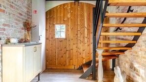 Eine Holztür mit Fenster, eine Treppe mit Holzstufen und ein heller Schrank mit einer Vase getrockneter Blumen.