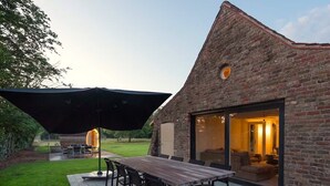 Ein Backsteinhaus mit einer großen Terrasse, einem Esstisch und einer überdachten Sitzgruppe.