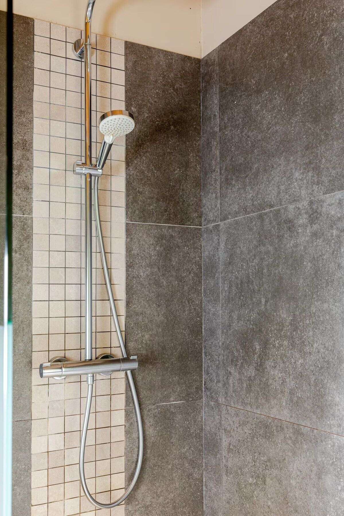 Una ducha con cabezal de ducha de mano y panel de control en la pared.