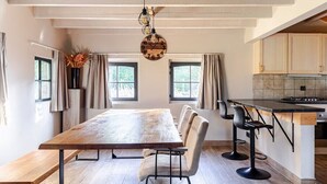 Eine moderne Küche mit Holztisch, Barhocker, großen Fenstern und einer Pendelleuchte.