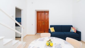 Ein Wohnzimmer mit einem blauen Sofa, einem runden Tisch mit einer blumigen Tischdecke und einer Treppe, die zu einer oberen Etage führt.