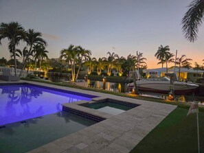 A swimming pool with a water feature, surrounded by palm trees and a boat docked by the water. - Waterfront House for 8 w Pool Near Las Olas (Wilton Manors)