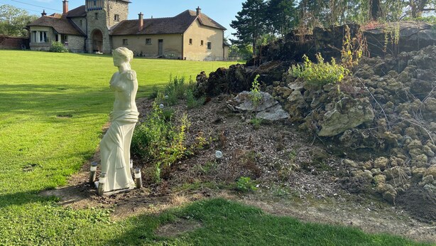 Une statue dans un jardin, avec un bâtiment en pierre en arrière-plan.