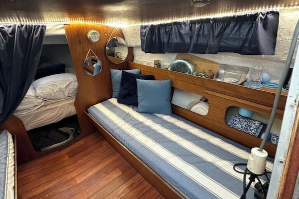 Un interior compacto y bien iluminado con una cama, un banco con cojines, un espejo y una mesita de noche con lámpara.