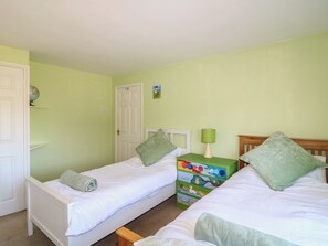 A room with two single beds, a wooden nightstand with a lamp, a colorful dresser, and a white door. - Highfields (Newark)
