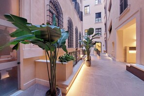 A narrow corridor with potted plants, a tiled floor, and a building facade with multiple windows and balconies. - Pirandello Luxury Home, in the prestigious Palazzo Raggi, in the heart of Rome (Roma)
