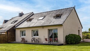 Une maison de plain-pied avec un toit en pente, un petit porche avec des chaises et une pelouse bien entretenue.