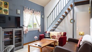 Un salon comprenant un canapé, une table basse, un téléviseur, une bibliothèque et un escalier.