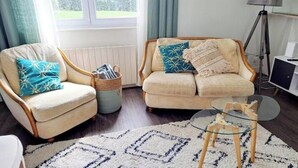 A living room with a sofa, armchair, and a small glass table. - Charming house with swimming pool (Tourville les ifs)