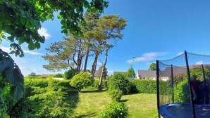 A backyard with a trampoline, trees, and a house in the background. - Charming house with swimming pool (Tourville les ifs)