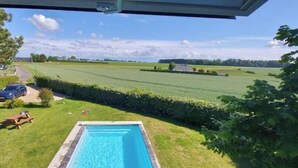 A swimming pool with a view of a green field and a car in the background. - Charming house with swimming pool (Tourville les ifs)
