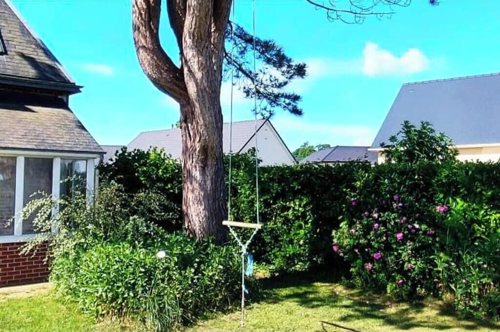 A residential area with a large tree, a swing set, and a house with a sloped roof.