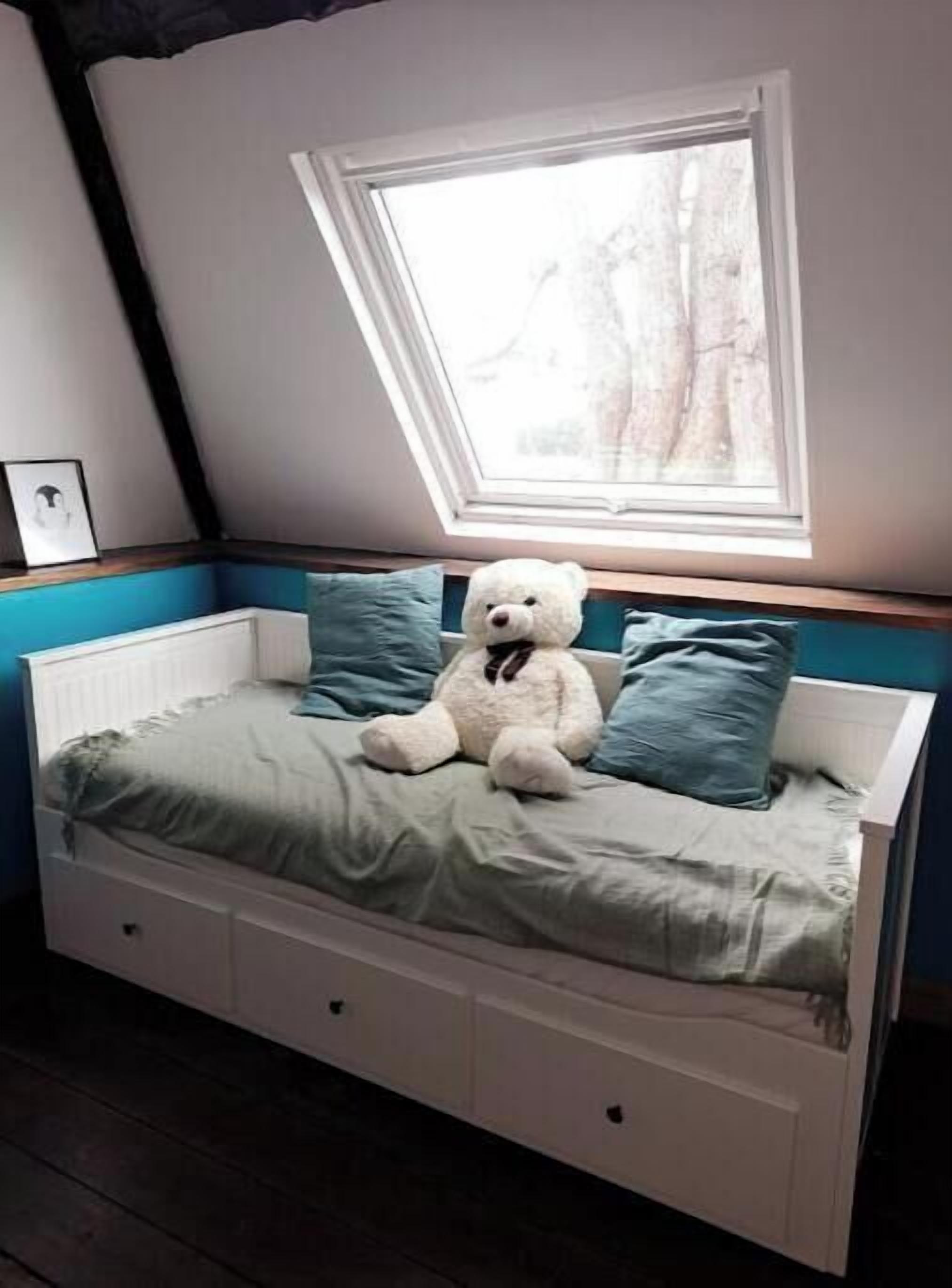 Ein Bett mit Dachfenster, einem Teddybären und blauen Kissen.