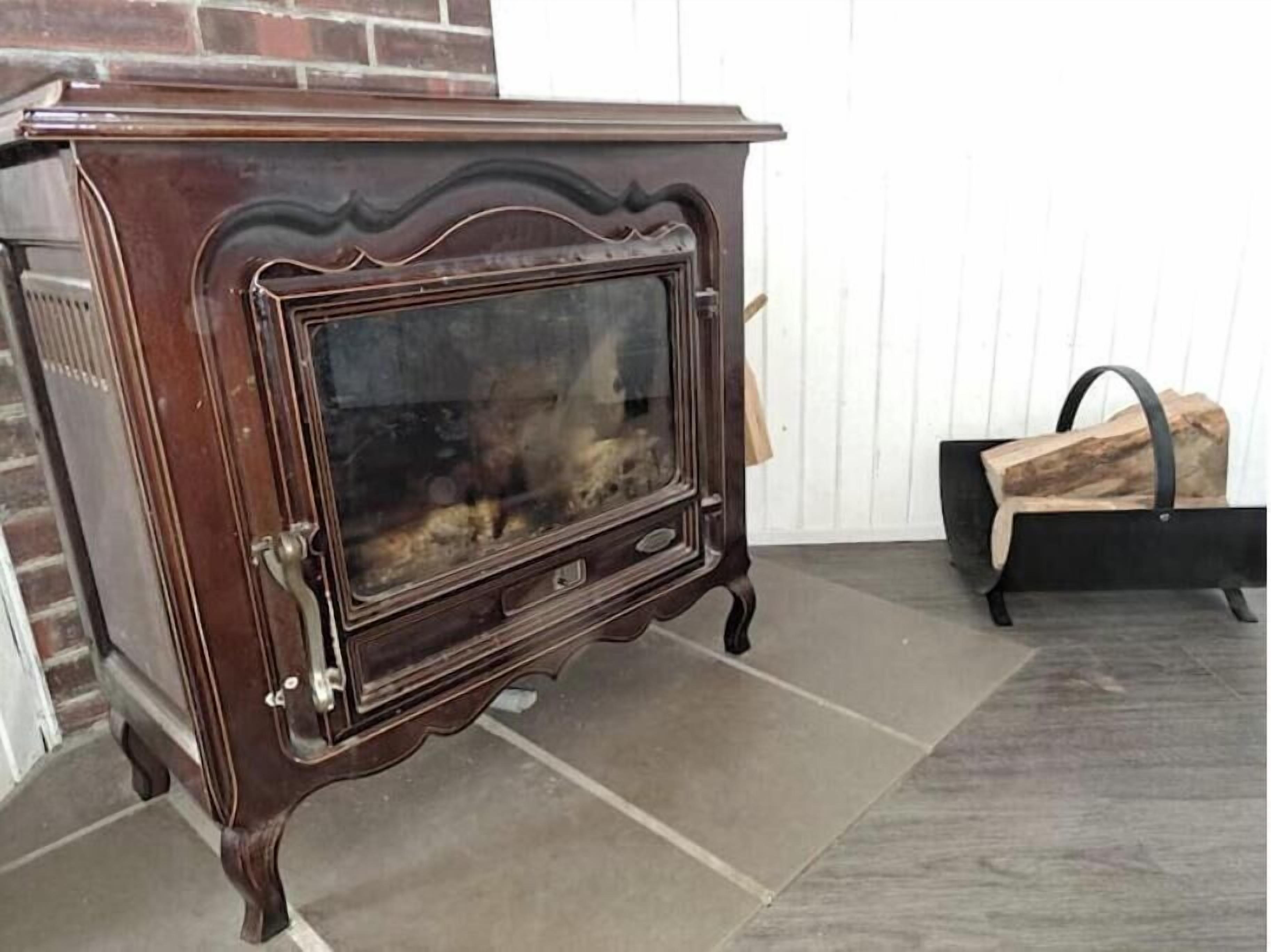A vintage stove with a glass door, a brick wall, and a wooden log holder.