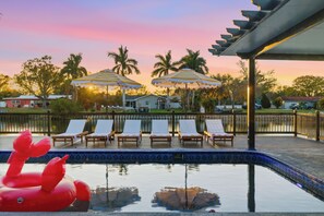 A pool area with lounge chairs and umbrellas, surrounded by palm trees and a sunset sky. - Waterfront Villa! Heated Pool, Paddle Boards, and Game Room, Sleeps 20! (Clearwater)