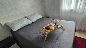 A neatly made bed with a tray of breakfast items, a bedside table, and a window with curtains.