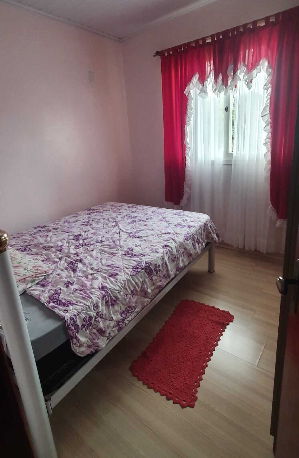 Um quarto com cama, tapete vermelho e janela com cortinas vermelhas.