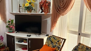 A living room with a TV, a cabinet with flowers, and two chairs with floral cushions.