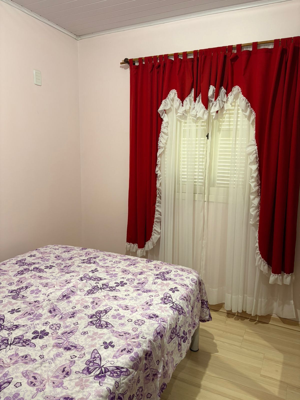 Une chambre à coucher avec un lit, des rideaux rouges, des rideaux blancs et une couvre-lit à motifs floraux.