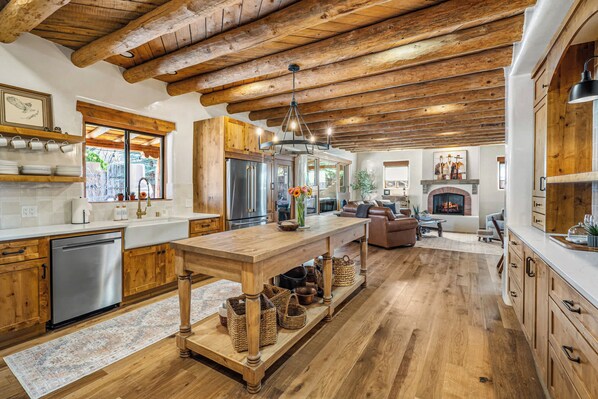 A spacious kitchen with wooden beams, a central island, and a fireplace in the background.