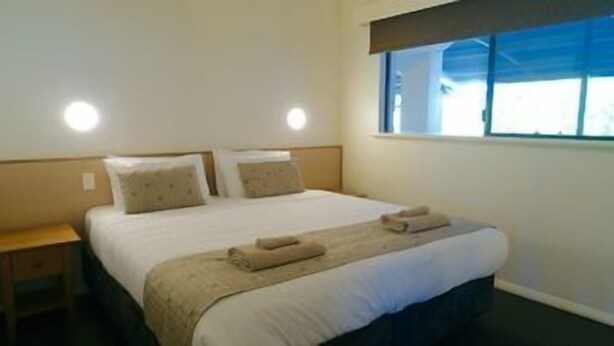 A hotel room with a bed, two bedside tables, a window with blinds, and a ceiling light. - Margaret River Beach Apartments (Gnarabup)