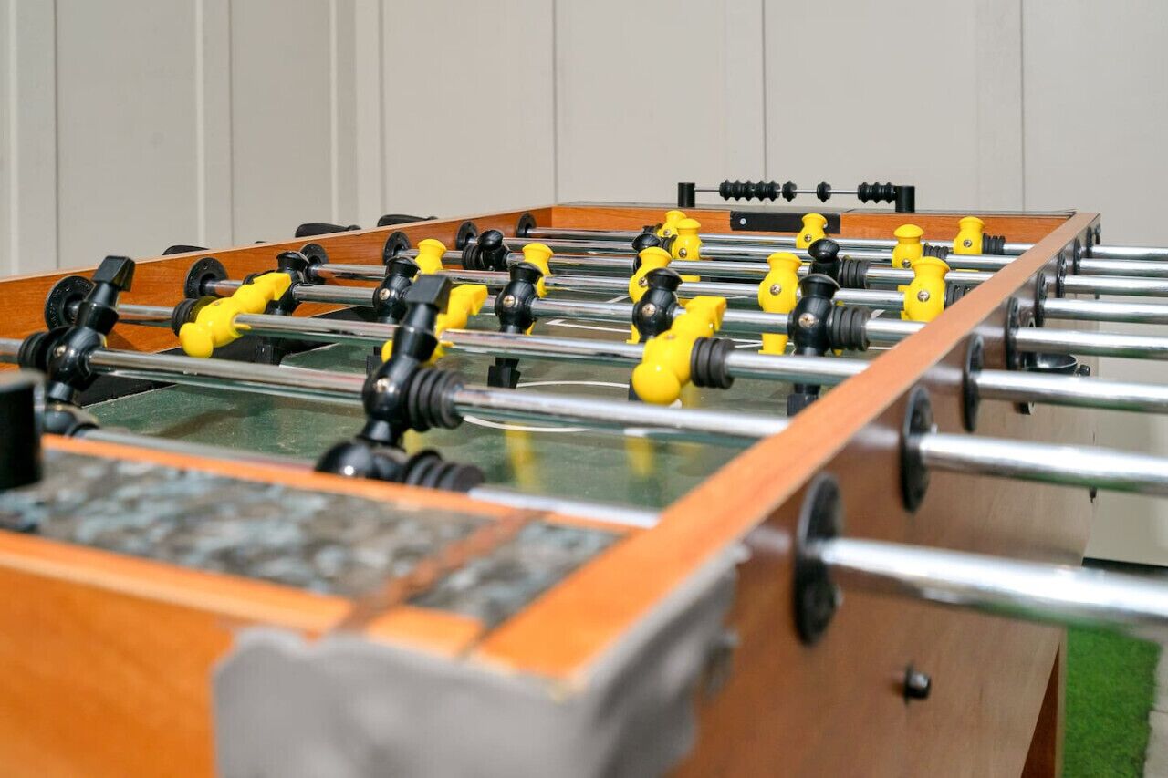 Une table de baby-foot avec des poignées jaunes et noires, un cadre en bois et une surface de jeu en verre.