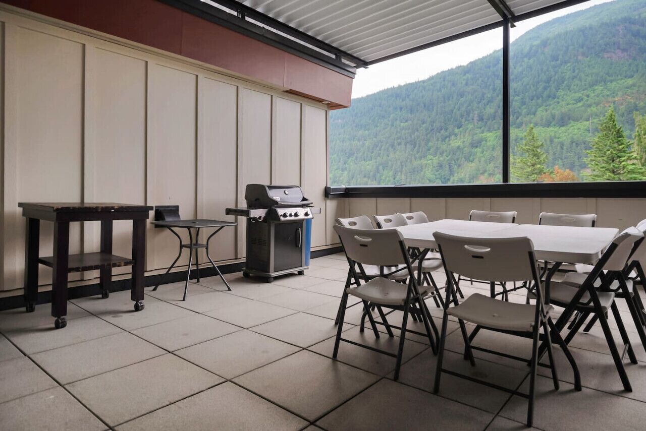 Un patio cubierto con una parrilla, mesa de comedor y sillas, con vistas a una montaña boscosa.
