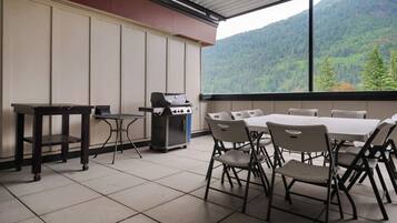 Un patio cubierto con una parrilla, mesa de comedor y sillas, con vistas a una montaña boscosa.