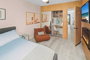 A hotel room with a bed, a brown armchair, a desk, and a TV. - Mission Hills 2BR | City Views & Covered Parking (San Diego)