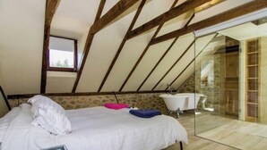 Een slaapkamer met een schuine kap, een bed, een raam en een badkamer met een bad.