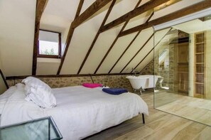 Une chambre avec un plafond en pente, un lit, une fenêtre et une salle de bain avec une baignoire.