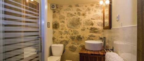 Ein Badezimmer mit Steinwand, Toilette, Waschbecken und Spiegel.