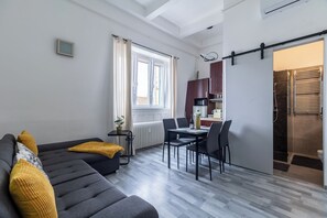 Ein modernes Wohnzimmer mit Sofa, Esstisch und Stühlen, einer Küchenzeile mit Schränken und einer Mikrowelle sowie einer Schiebetür zu einem Duschbereich.