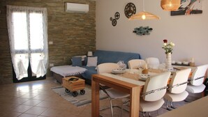 Een moderne woonkamer met een bank, eettafel, stoelen en een kleine kar.