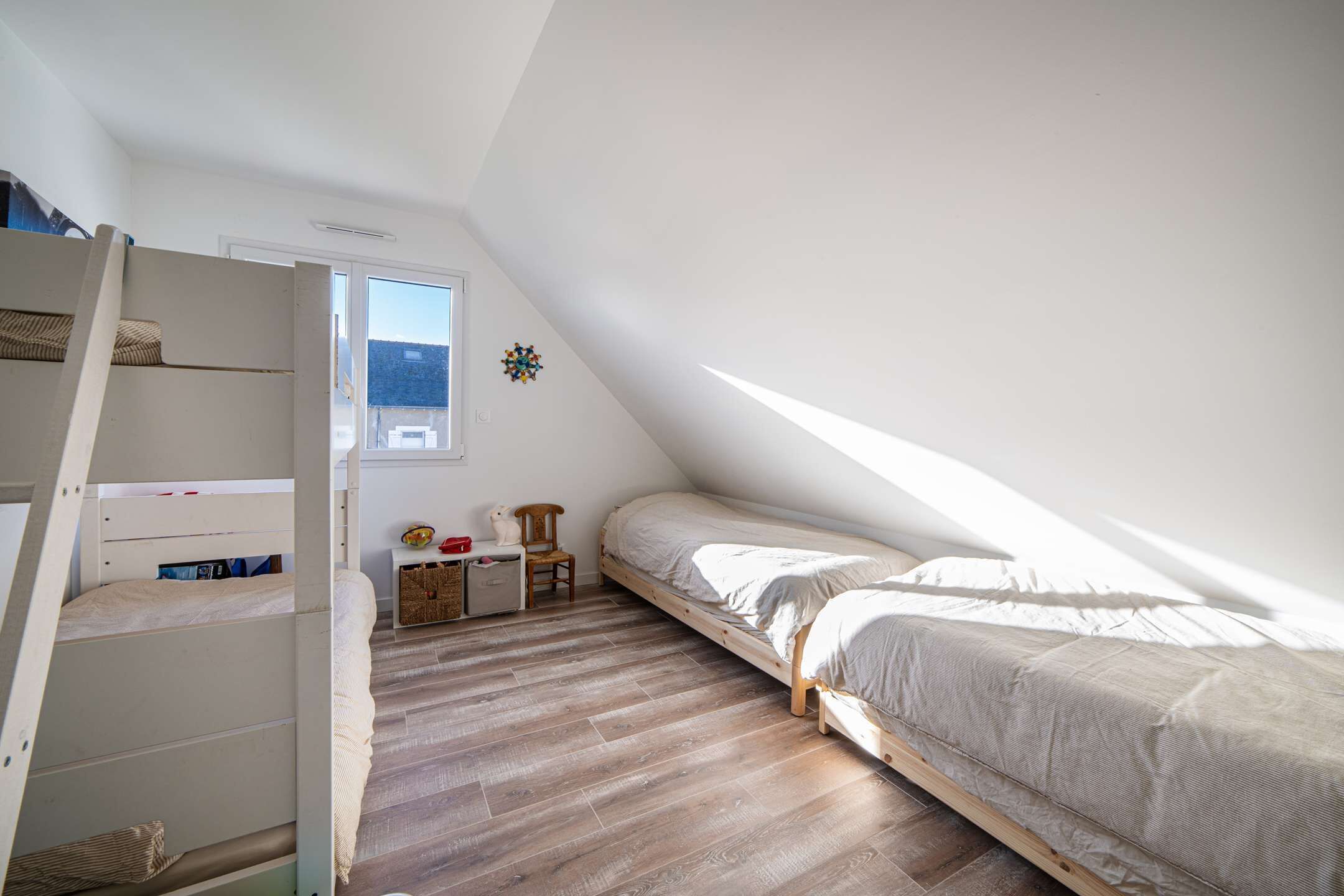 A dorm-style room with bunk beds, a desk, chair, and a small window.