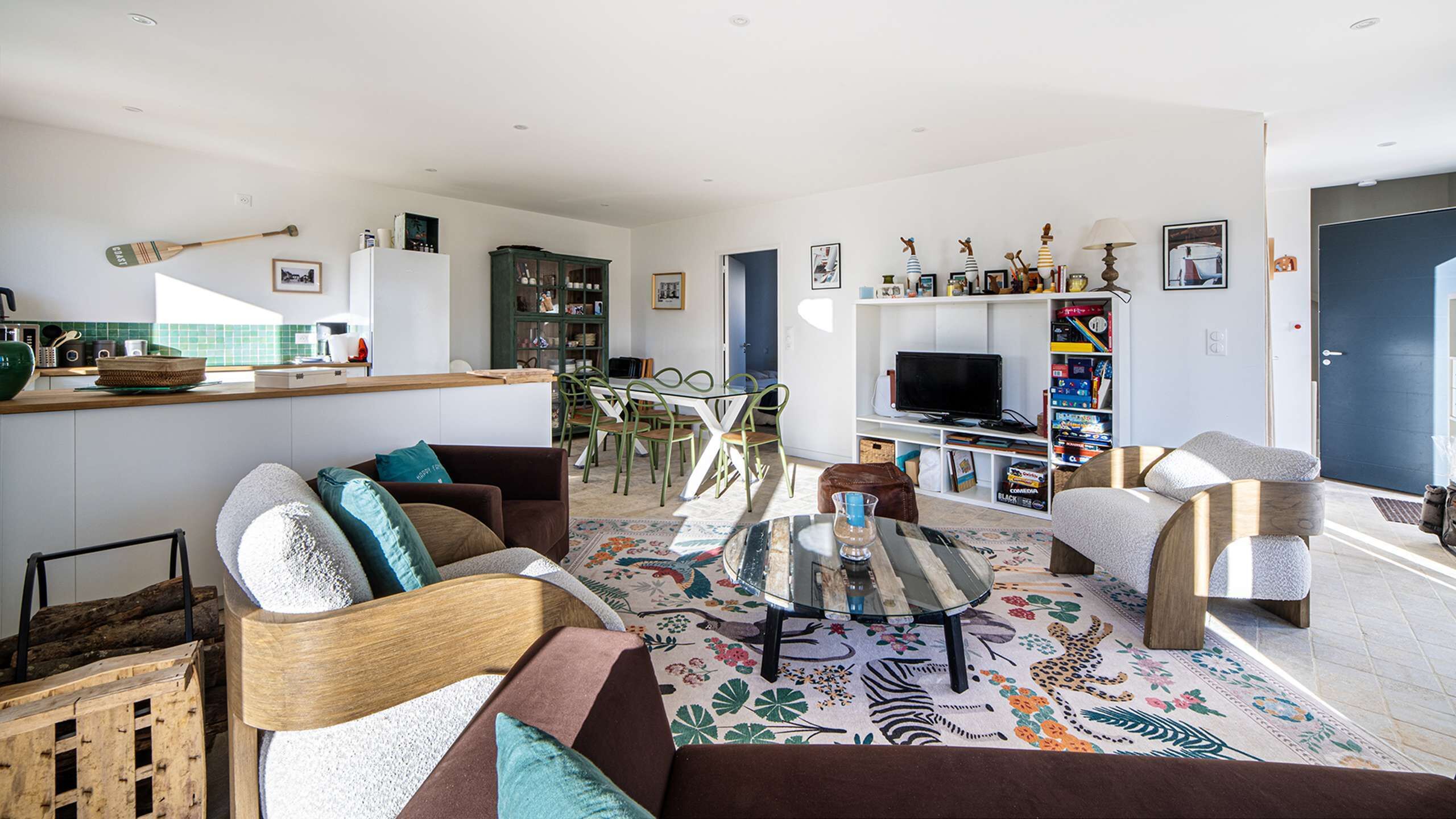 Una sala de estar moderna con una mesa de centro de vidrio, un sofá y un televisor. Hay una zona de cocina con mostrador y una mesa de comedor con sillas.