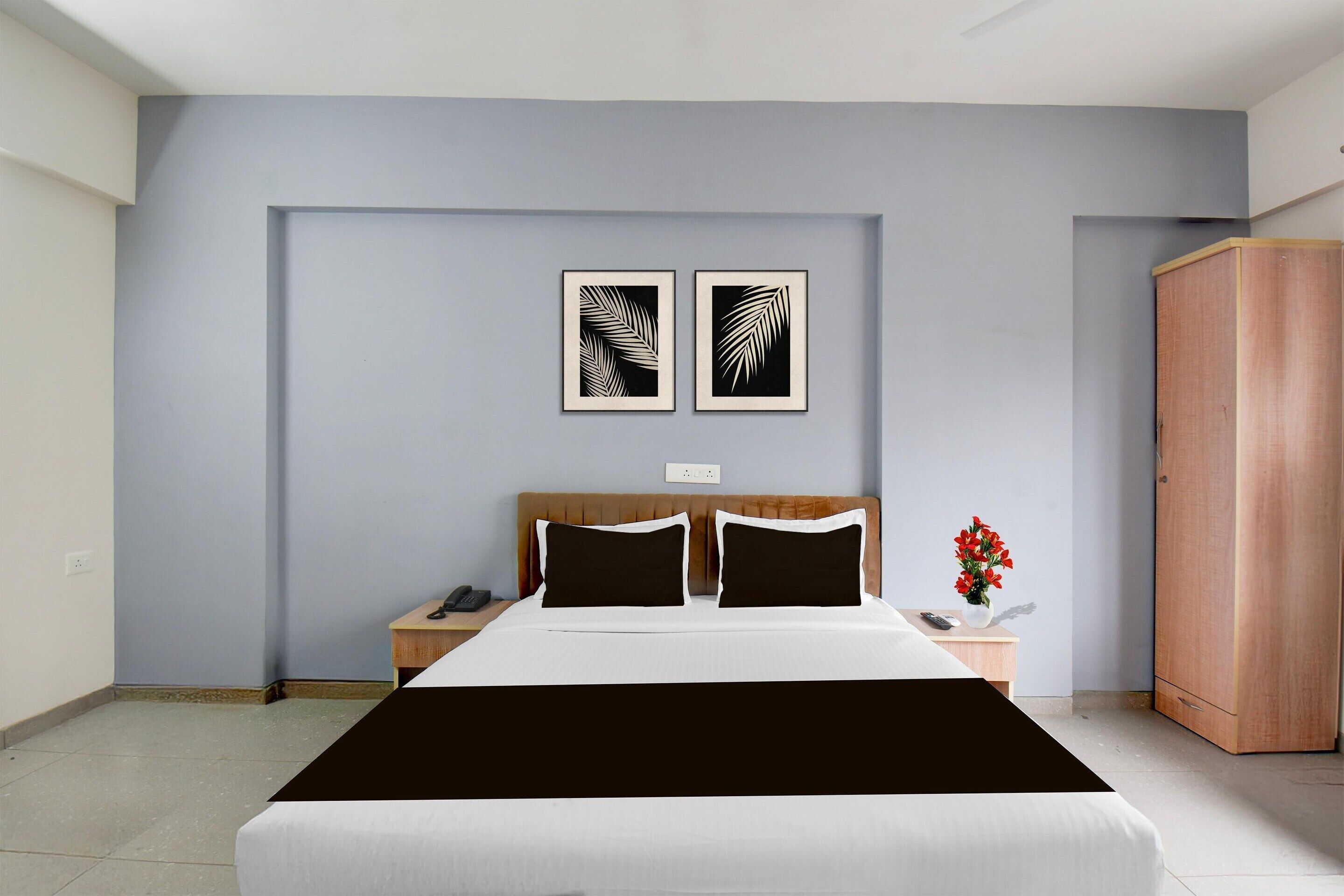 Habitación de hotel con cama, mesita de noche, armario y dos obras de arte con hojas enmarcadas en la pared.