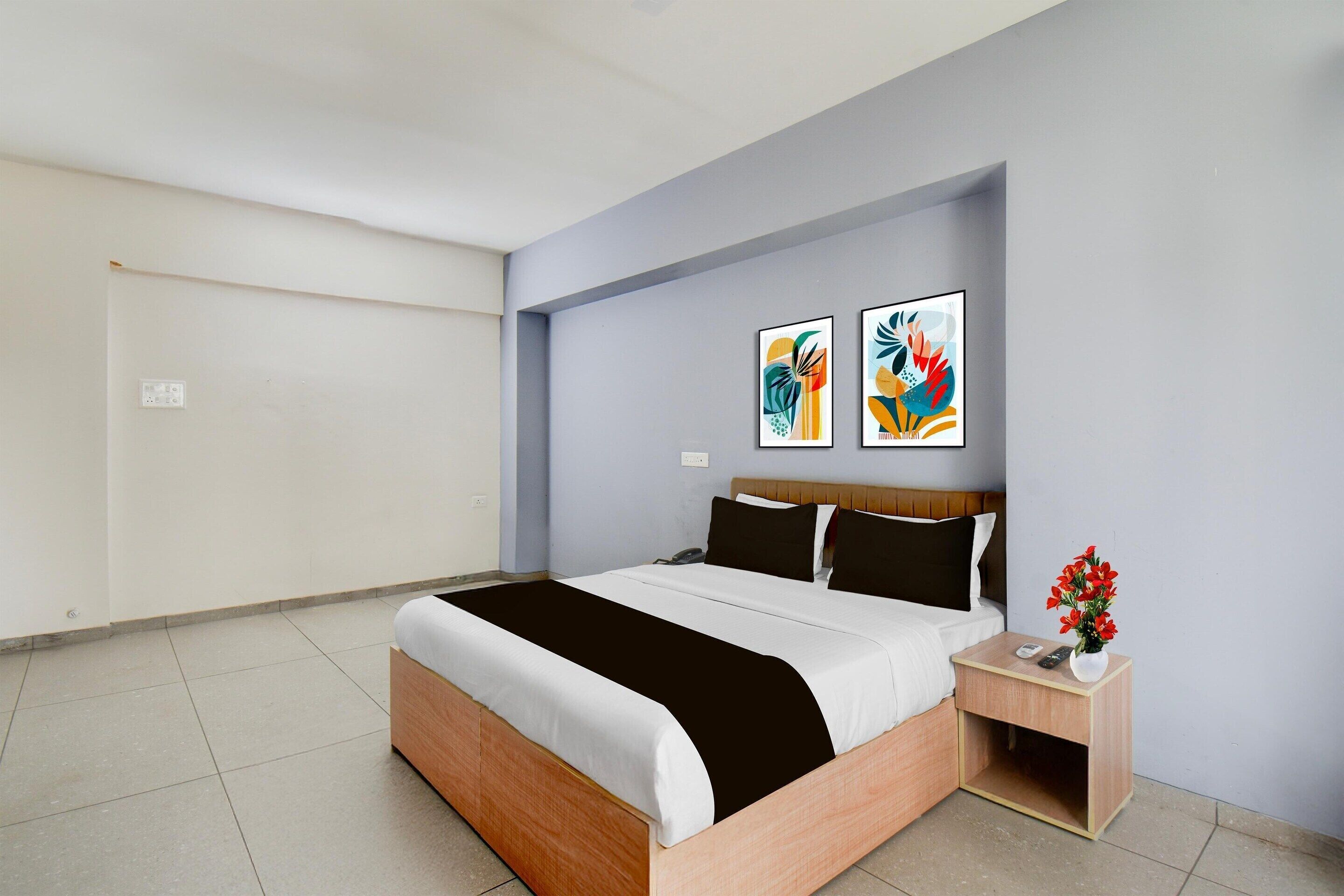 A modern hotel room with a bed, bedside table, and two abstract paintings on the wall.