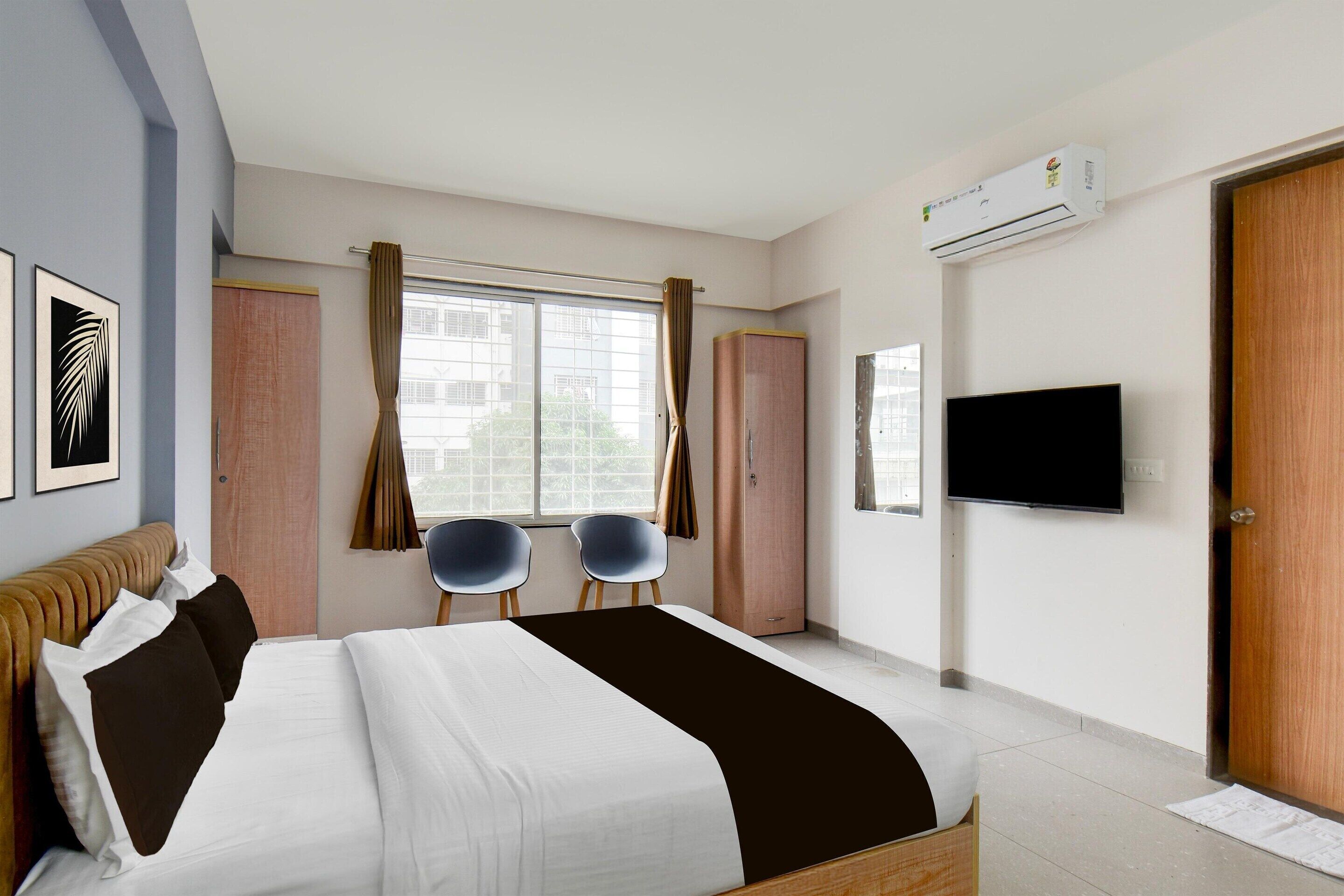 Habitación de hotel con una cama, dos sillas, un televisor, aire acondicionado y una ventana con cortinas.