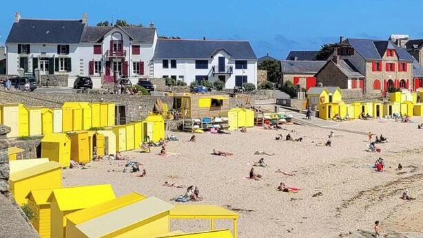 Una playa con estructuras amarillas, un muro de piedra y edificios al fondo.
