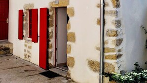 Un bâtiment doté d’une façade en pierre, d’une porte rouge et d’une fenêtre avec des volets rouges.