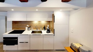 A modern kitchen with white cabinets, a black countertop, a wooden backsplash, and a built-in oven. - Le clos du prieuré - Les Gîtes de la Côte d'Amour (BATZ SUR MER)