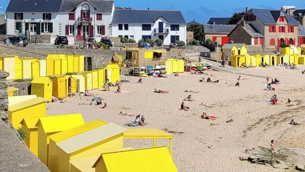 A beach with yellow structures, a stone wall, and buildings in the background. - Le clos du prieuré - Les Gîtes de la Côte d'Amour (BATZ SUR MER)