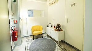 Habitació d'hotel amb un extintor, una cadira groga, una consola blanca i una porta amb un símbol familiar.