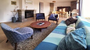 Una sala de estar con un sofá, dos sillones, una mesa de centro, una chimenea y un comedor con una mesa y sillas.