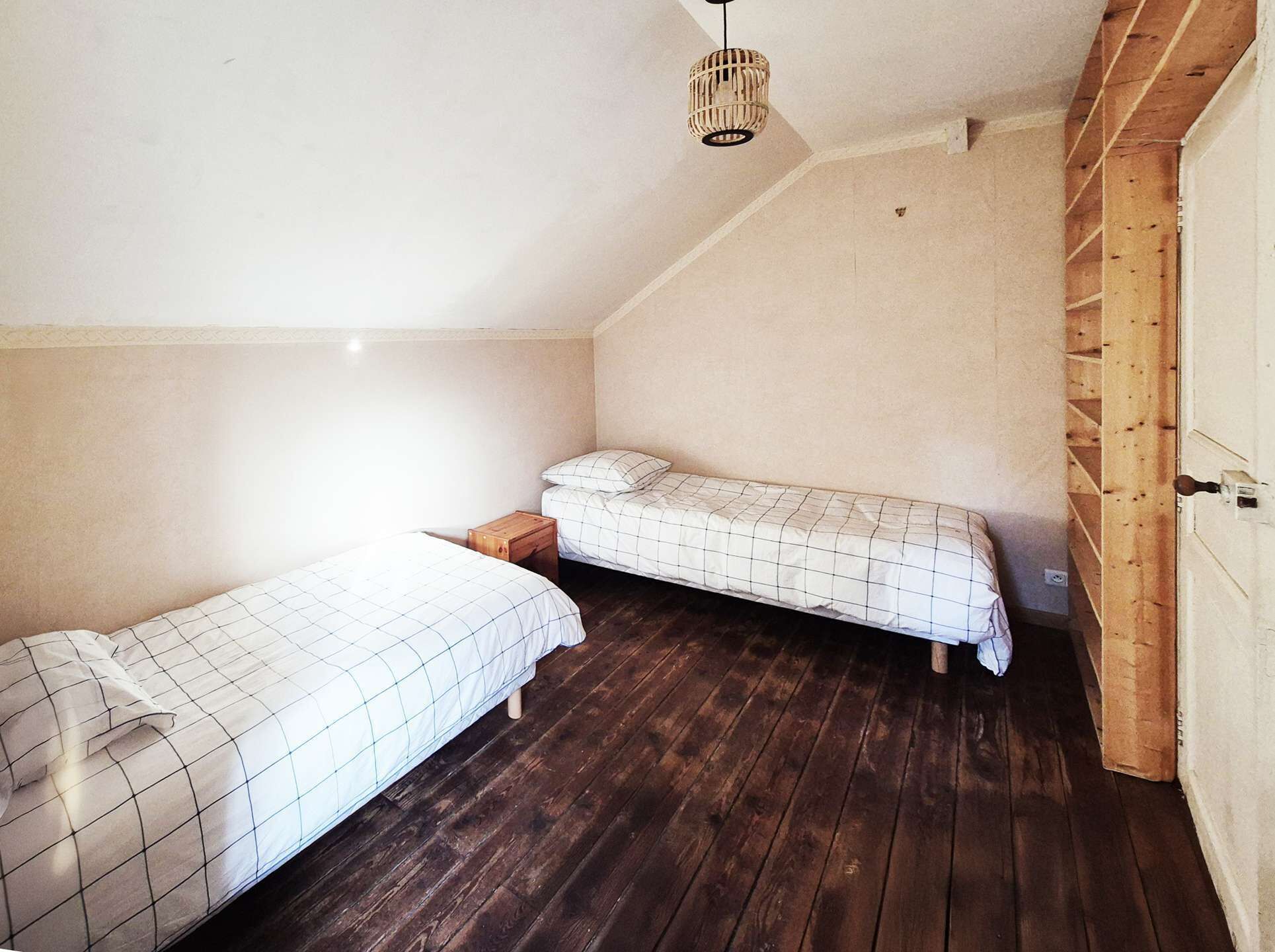 A small, single-bedroom room with two beds, a wooden floor, and a sloped ceiling.