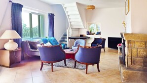 Una sala de estar con un sofá, dos sillones, una mesa de centro, un televisor, una chimenea y una escalera.